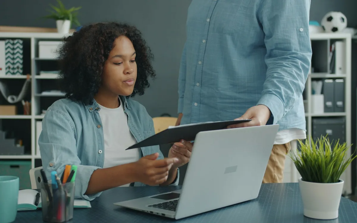Two colleagues reviewing a document beside a laptop
